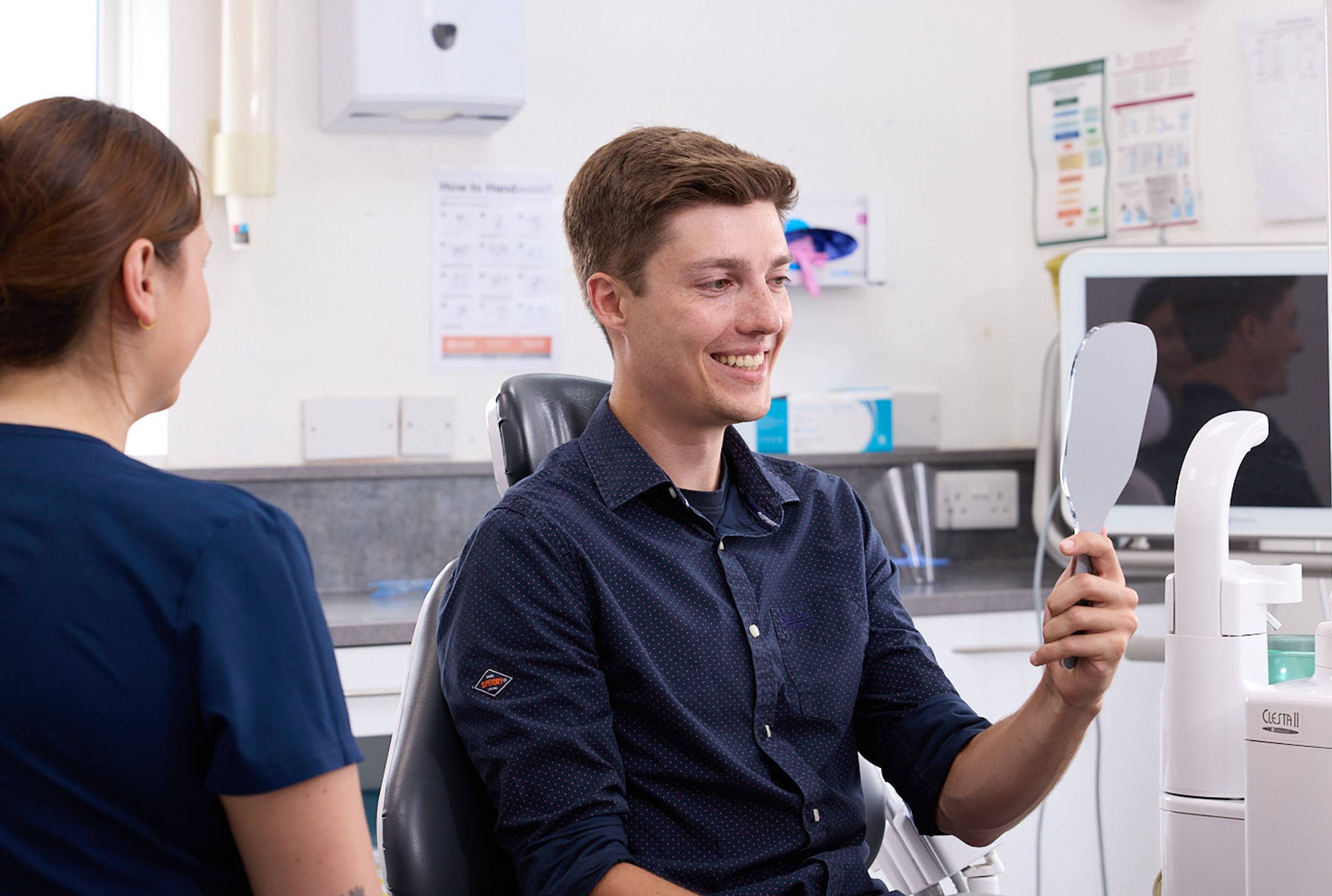 patient holding up mirror in dental surgery after treatment