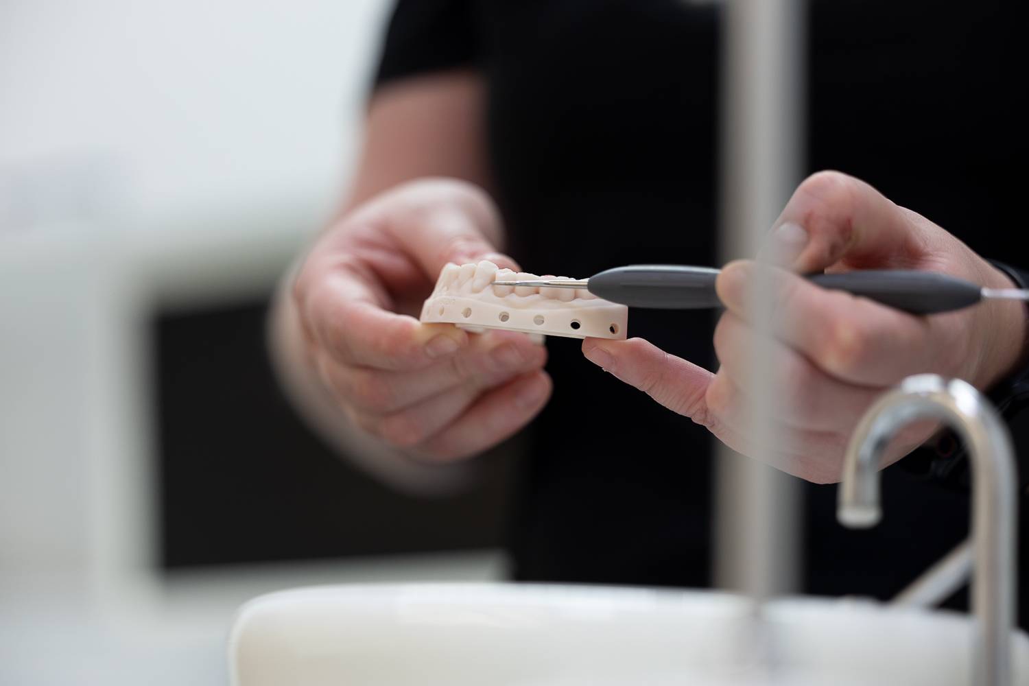 close up on dentist hands holding model lower set of teeth and dental implement showing example of bridge treatment