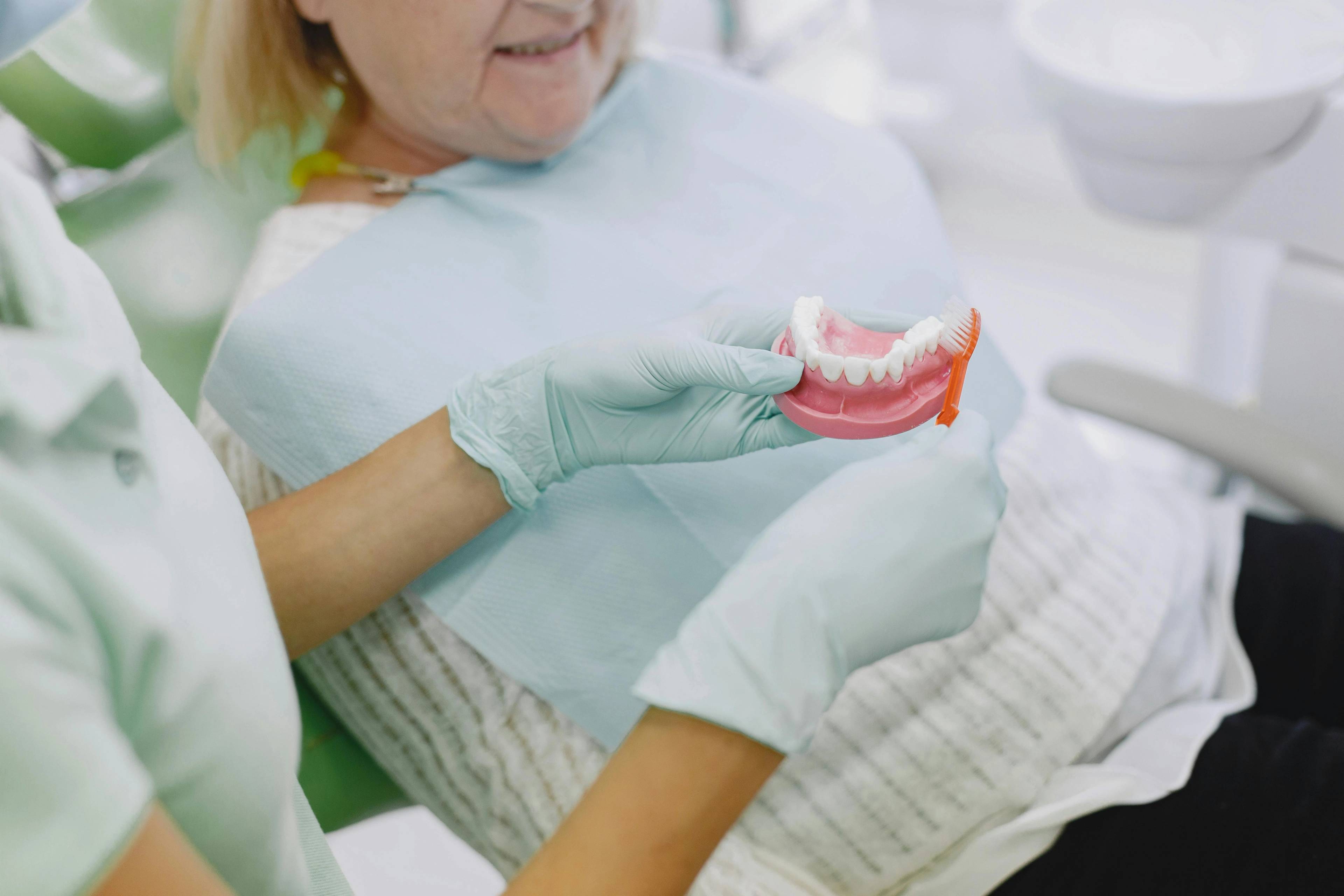 dentist holding model showing patient proper tooth brushing technique to help avoid fillings in the future