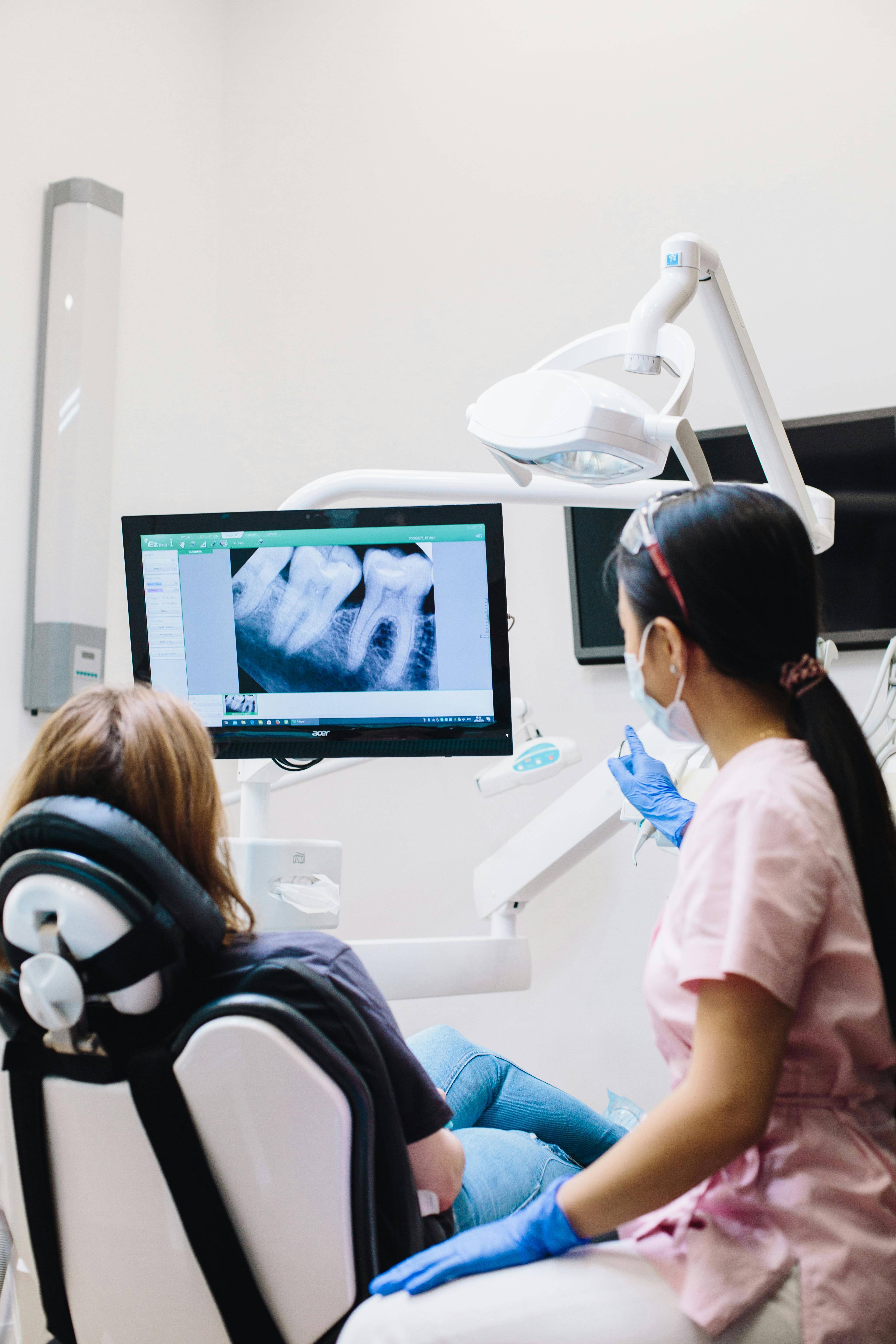 back of dental chair where patient sits looking at x-ray on screen as dentist points to discuss prognosis
