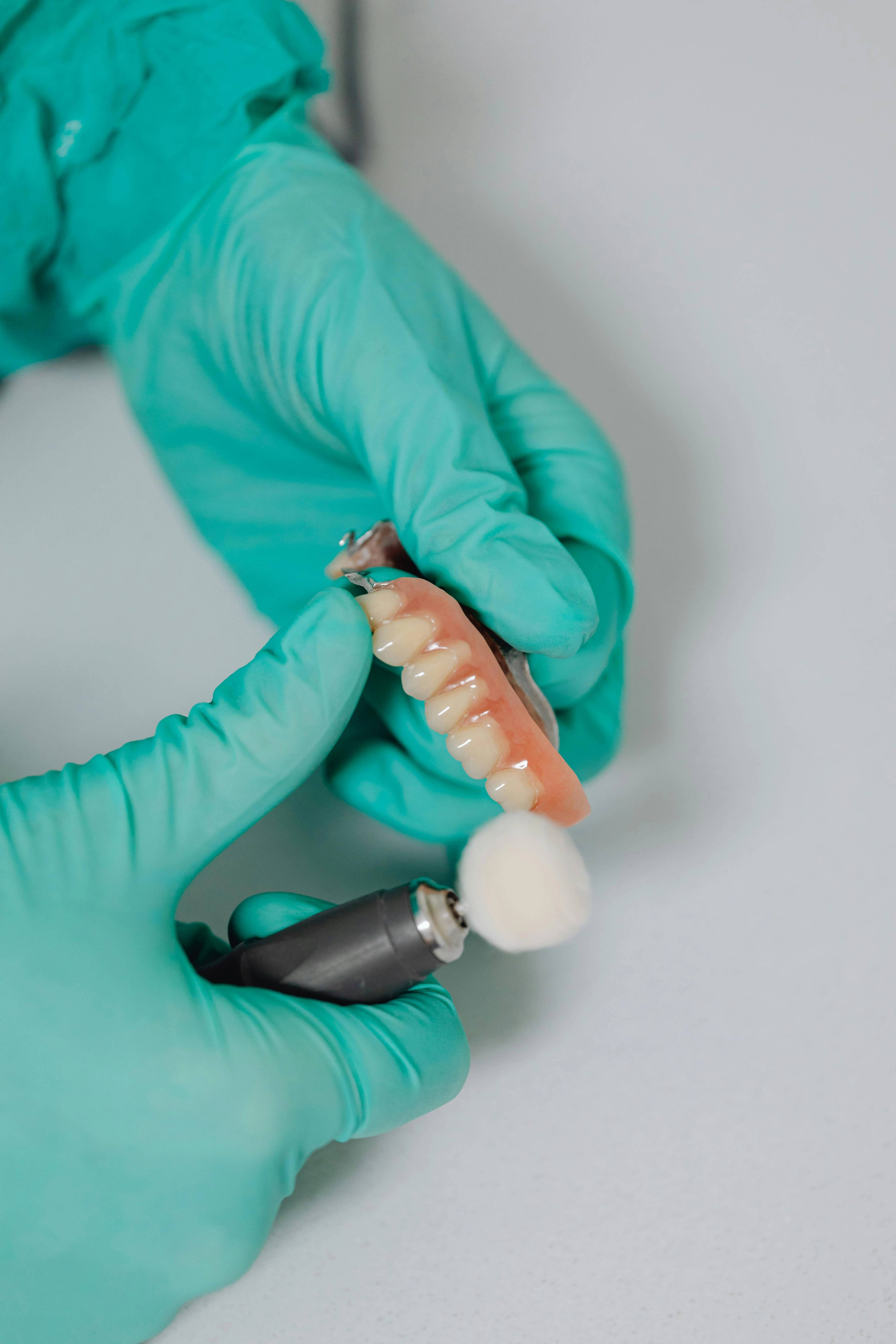 close up of dentist hands wearing green gloves as they use a tool to smooth edges of denture