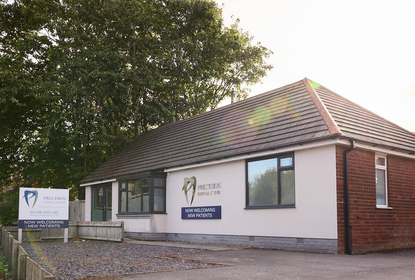 Outside precision dental clinic on a sunny day featuring front door signage and tree in car park