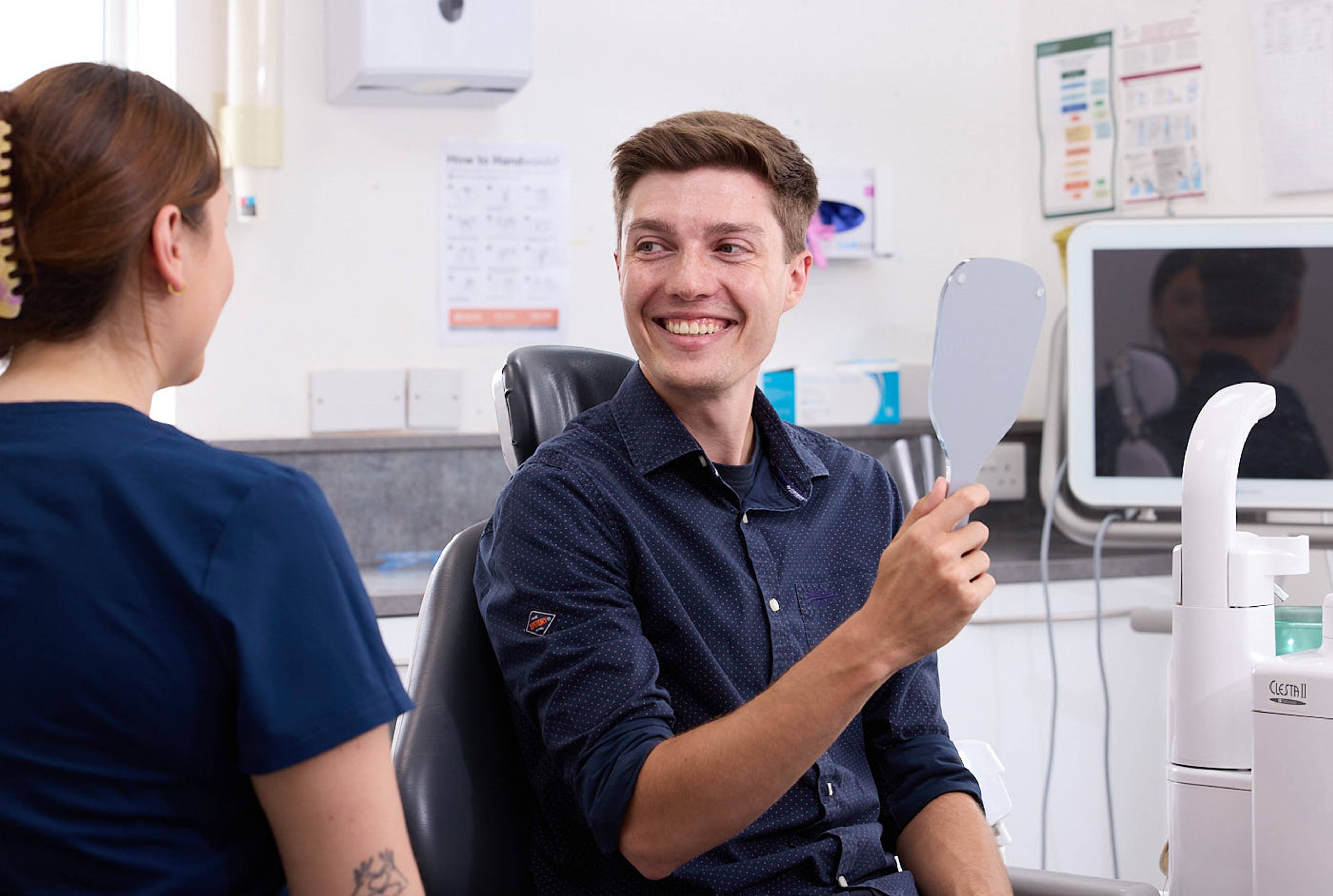 young man smiling holding mirror looking at dental nurse after sport mouth guard fitting