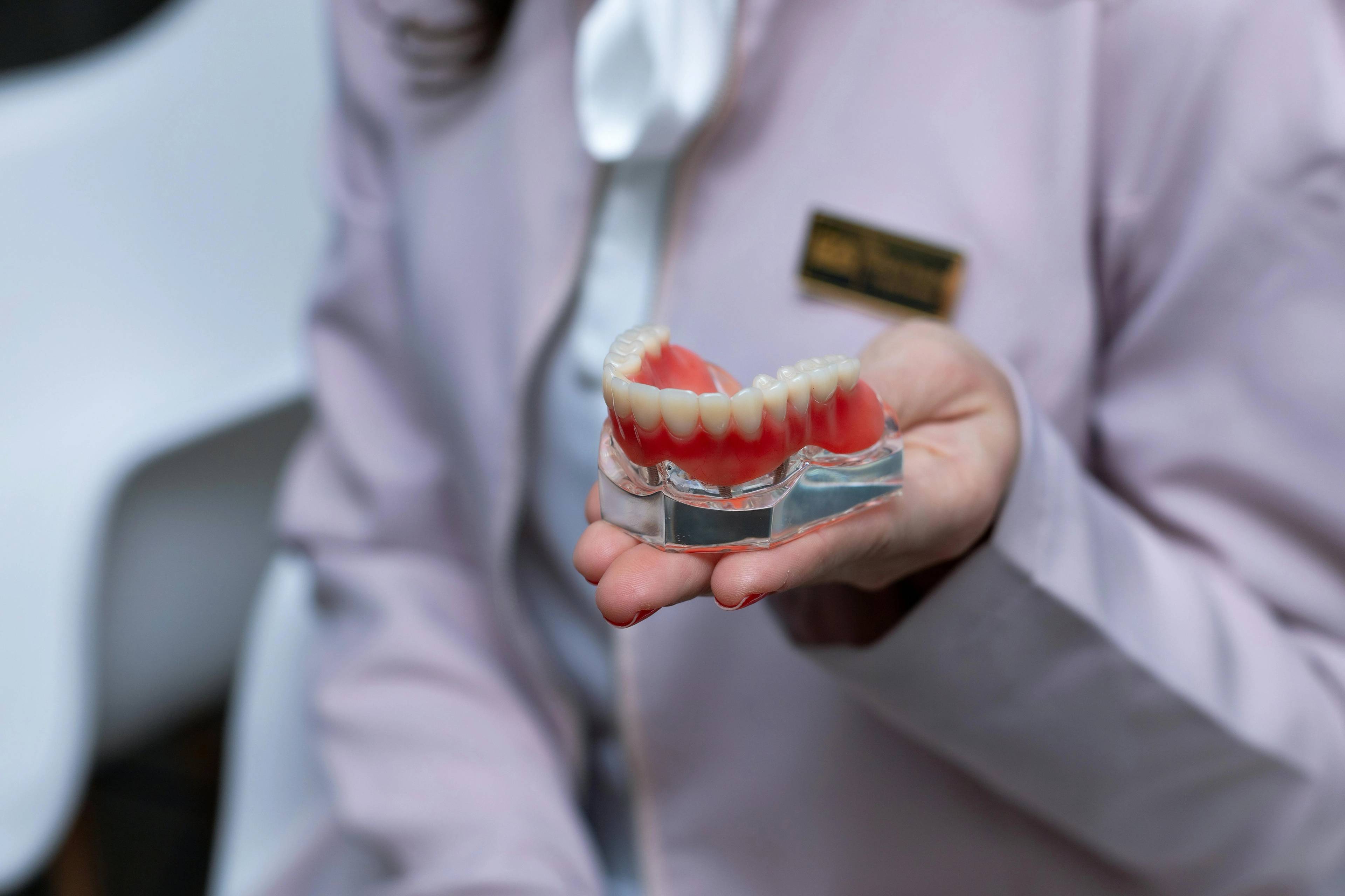 dentist holding a glass stand with a full denture resting on top before denture is fitted
