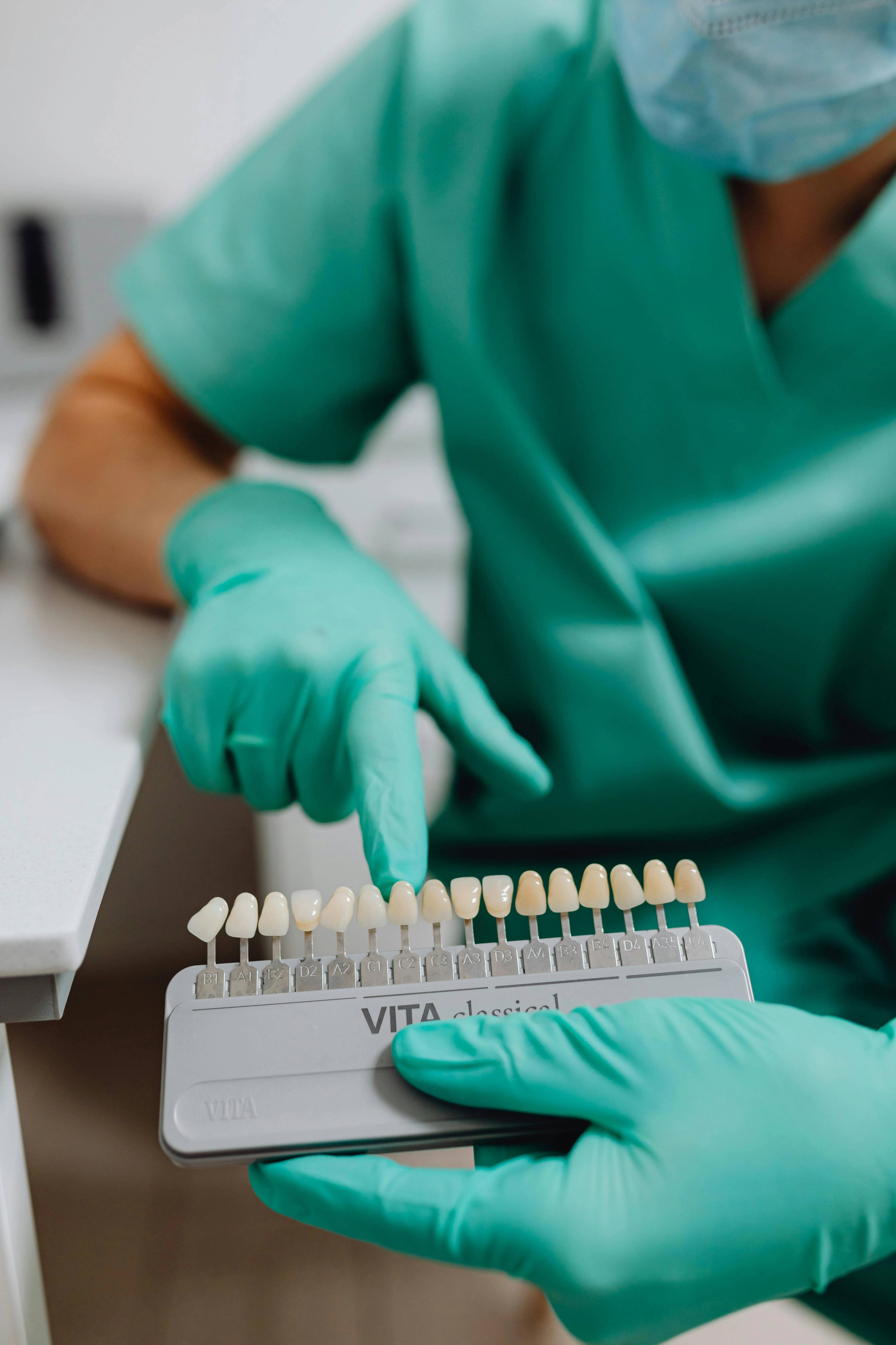 dentist wearing blue uniform and gloves showing variety of example shades of teeth on model