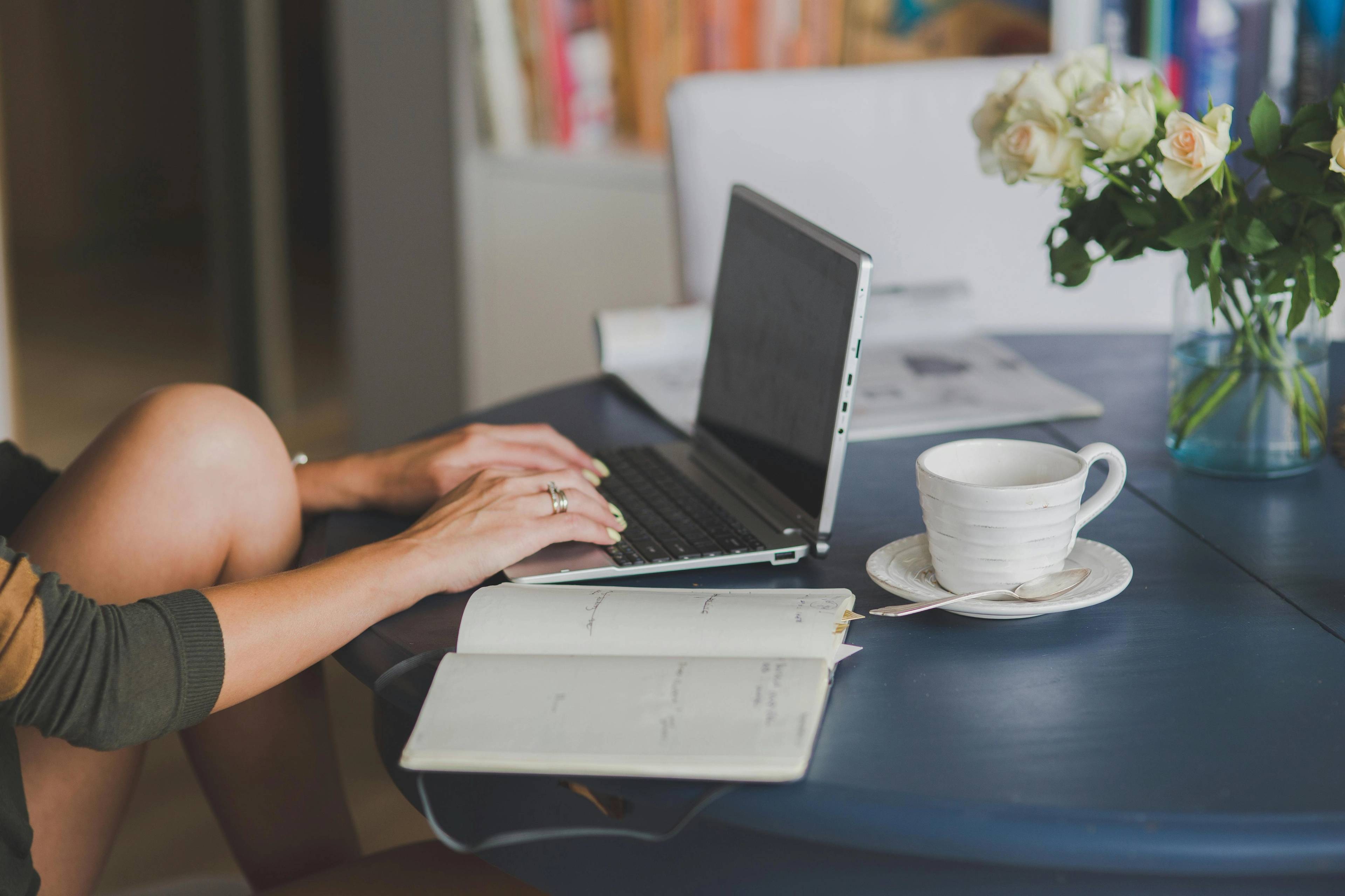 close up of person sat at laptop at a desk with coffee and a notepad applying for flexible finance for dental treatment