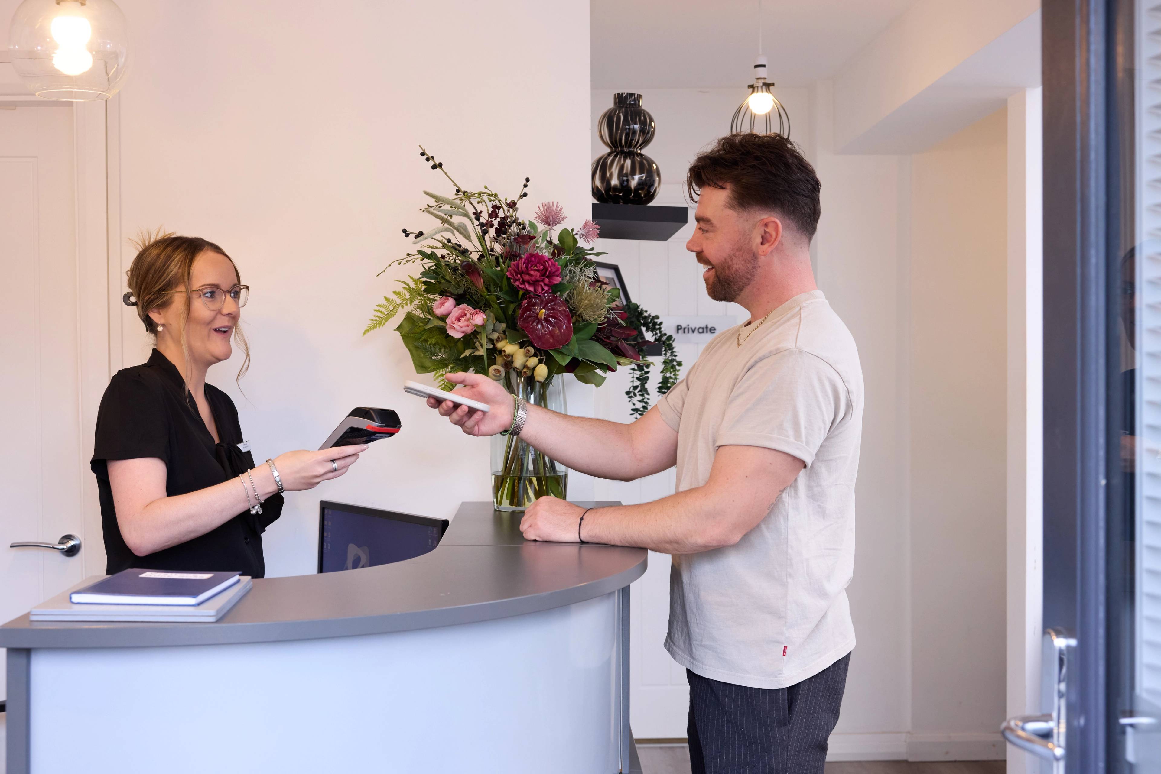 female receptionist taking payment from male patient at customer help desk featuring a vase of flowers in the background
