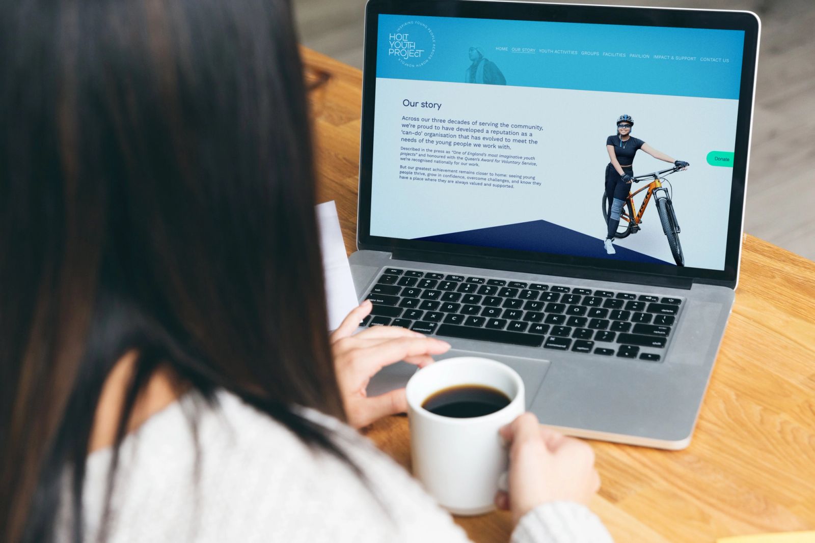 Woman drinking coffee looking at macbook screen