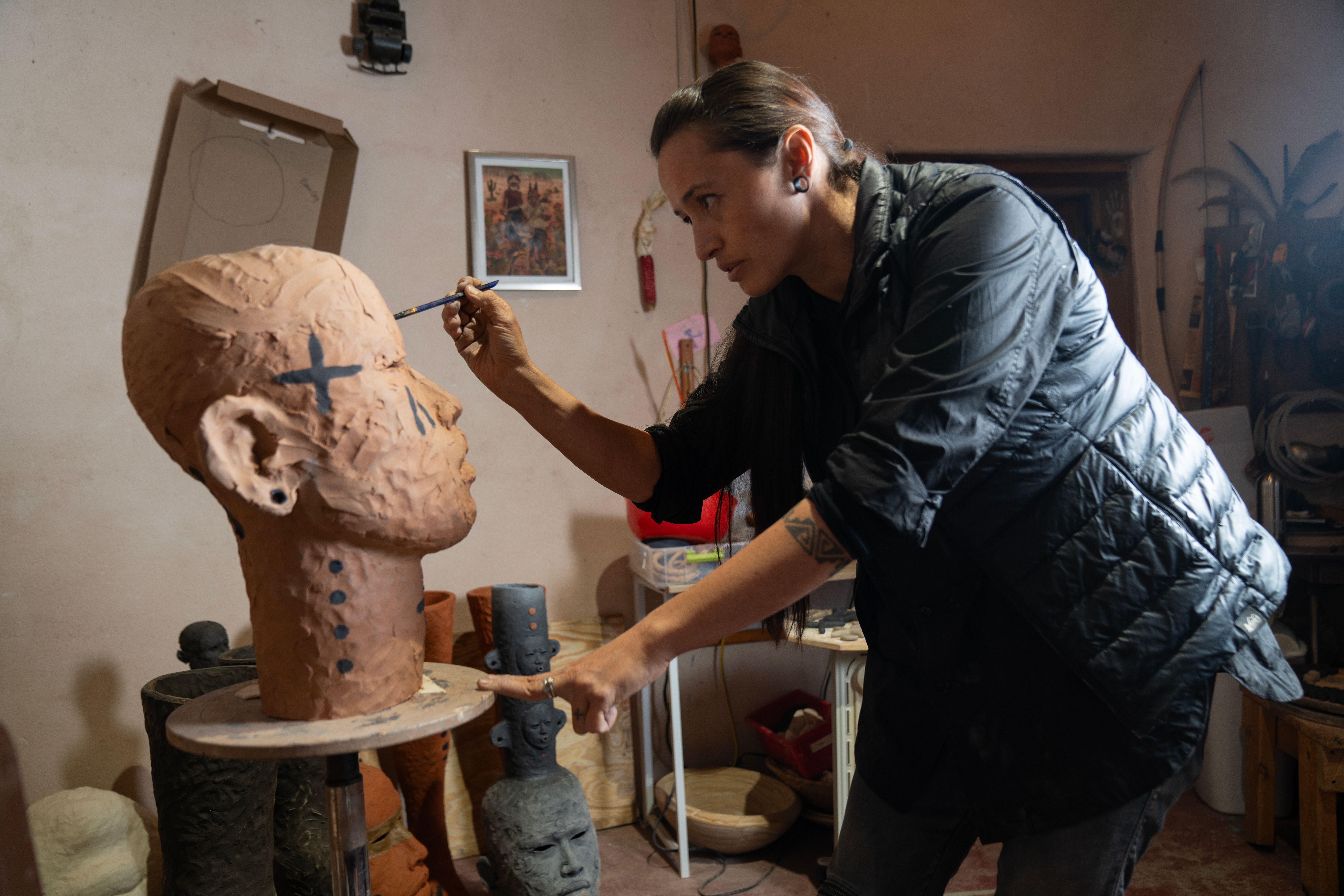 A wide shot of Rose painting the face of an extra large clay head