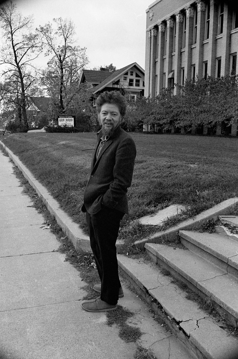 Black-and-white photograph of Benny Andrews standing on a sidewalk