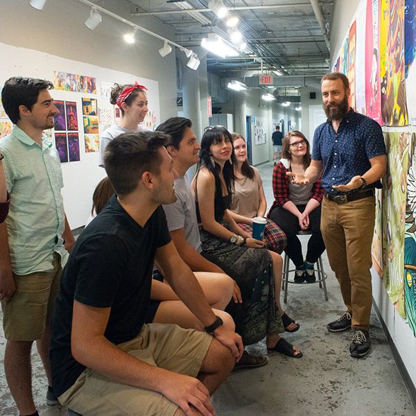 Group of students standing and seated around a piece of art during a critique session.