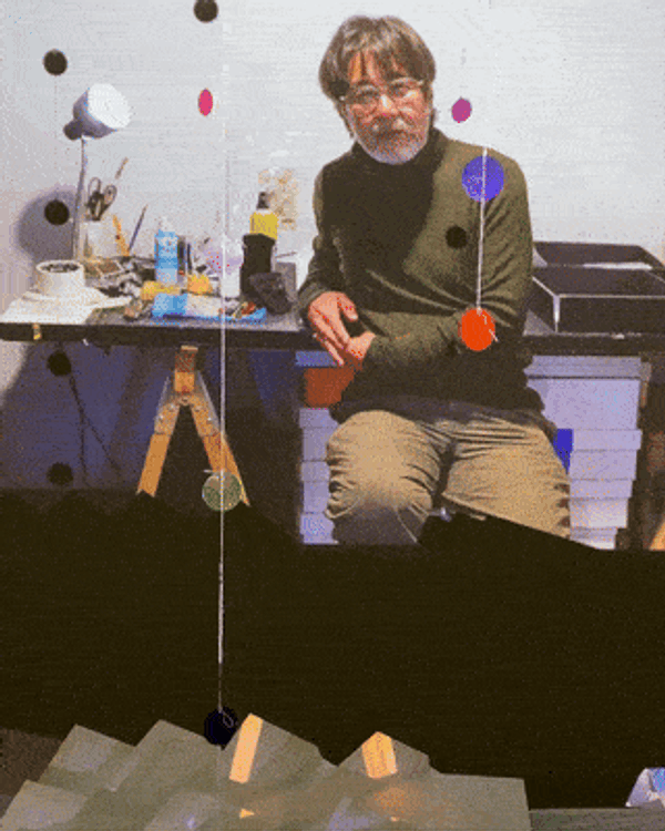 portrait of Yuji Agematsu in his studio, surrounded by stacks of books, crates, and other materials