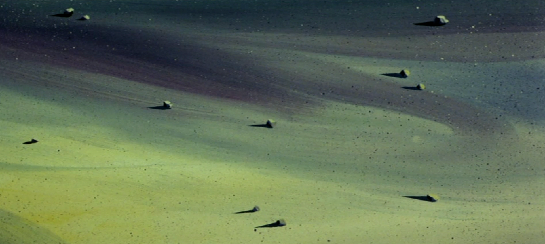 Detail of a painted seafloor from the 1975 Toei animated film The Little Mermaid: small shells scattered across sand washed in soft bands of green, yellow, and violet, each casting a long shadow.