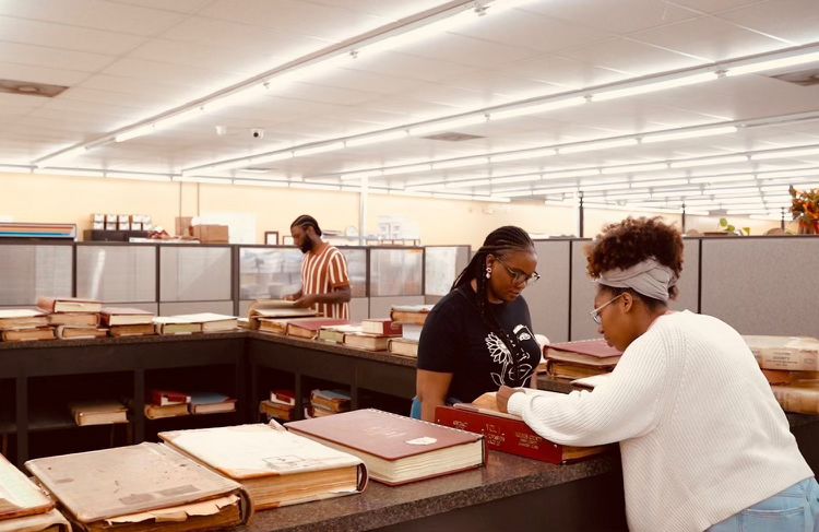 three individuals looking through archival materials in an office-like environment