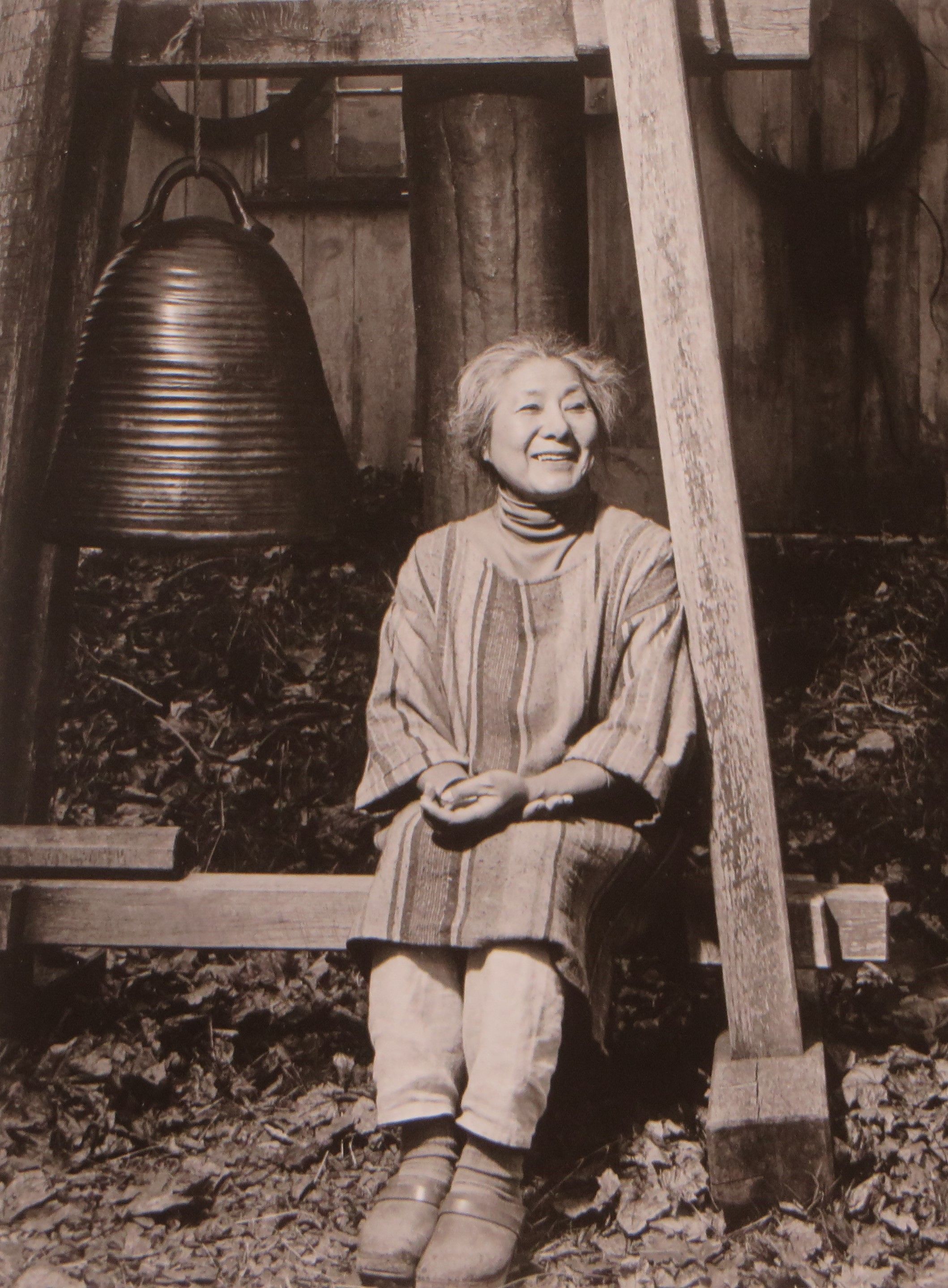sepia toned photgraph of Toshiko Takezu seated next to a large bell outdoors