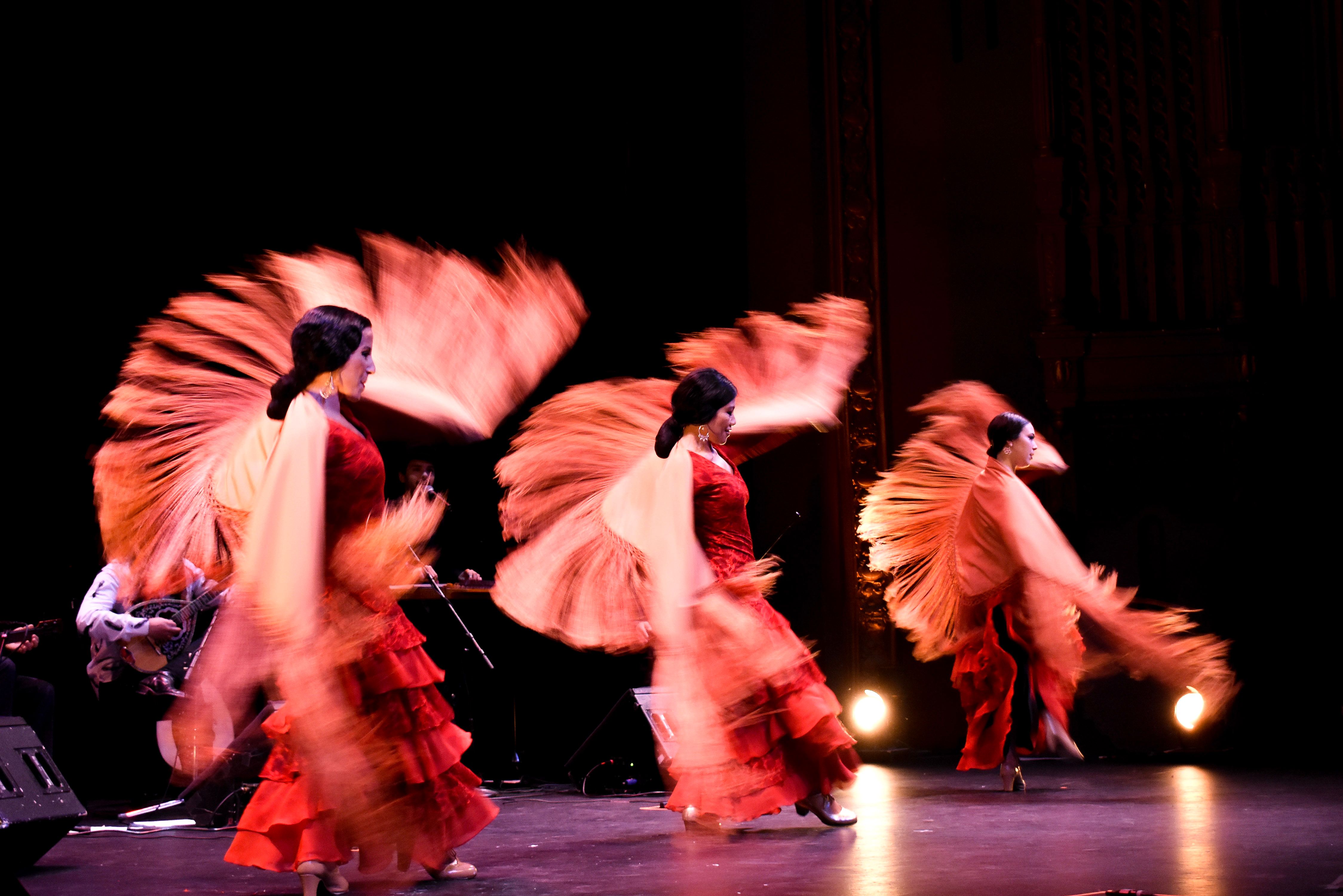 Three Flamenco dancers with their costumes bluured in motion around them, onstage
