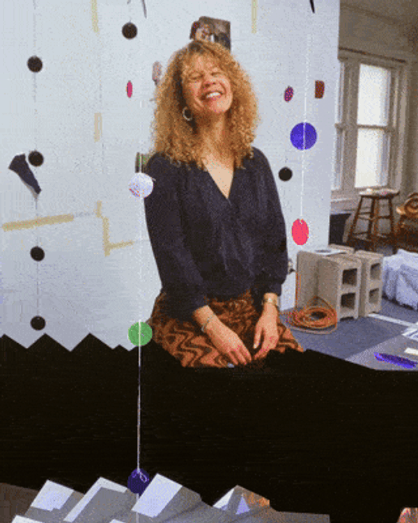 portrait of Anna Martine Whitehead, seated on a stool and smiling in her studio