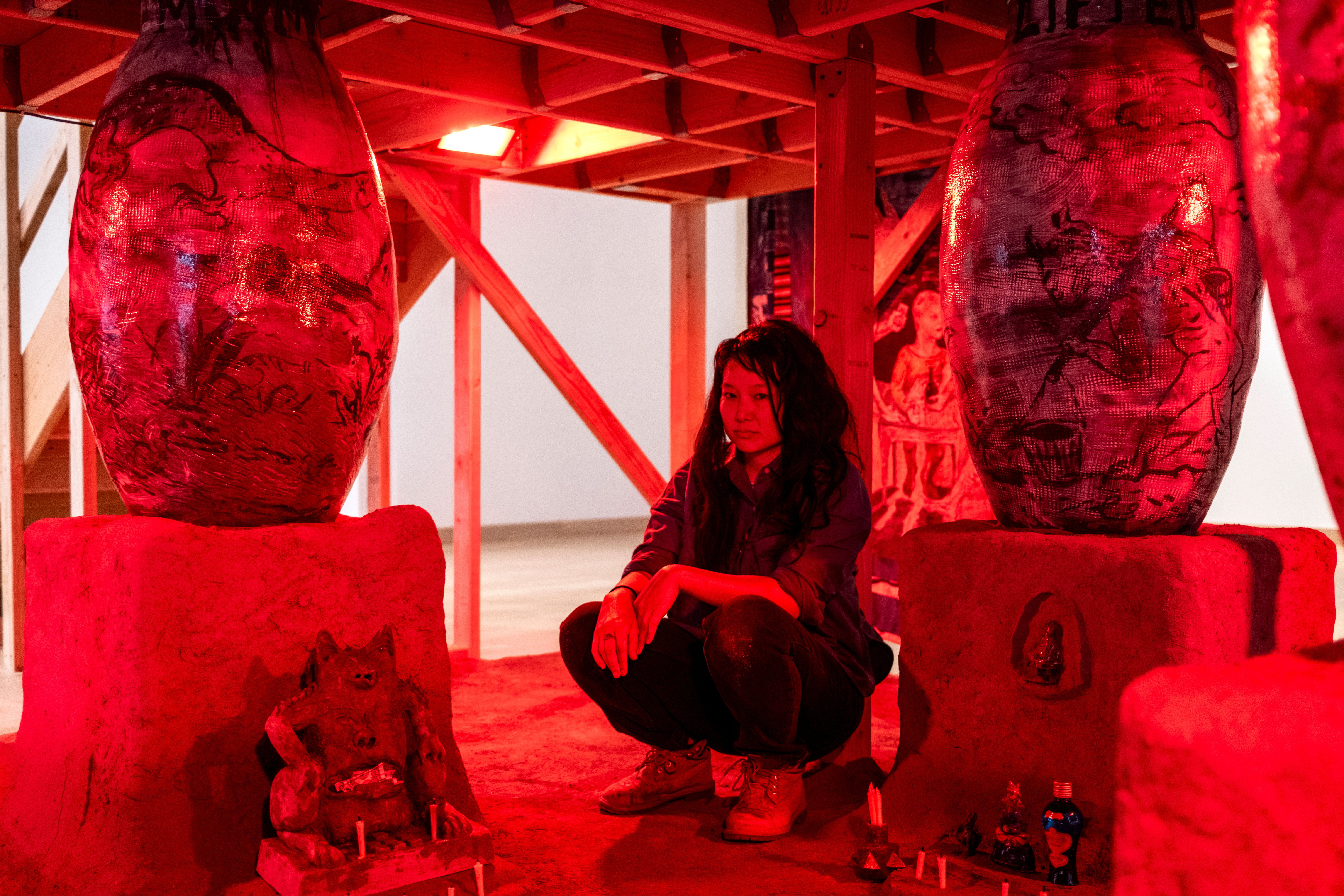 Candice Lin, crouched between two monumental ceramic sculptures under red light 