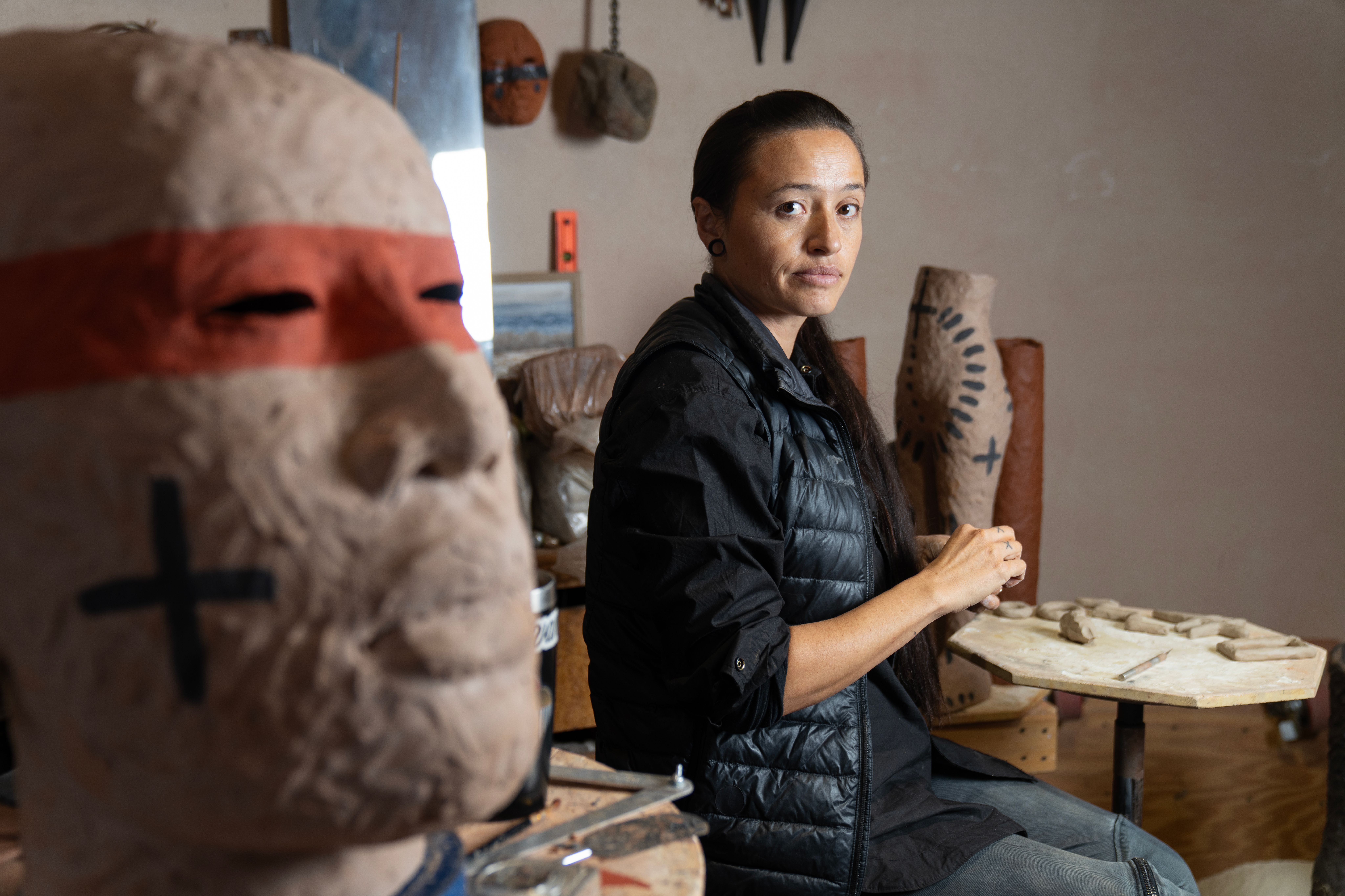 portrait of Rose B Simpson in her studio, looking at camera with a clay bust in the foreground