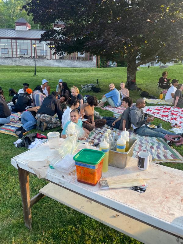 Artists share a meal outdoors on a summer day on quilted picnic blankets