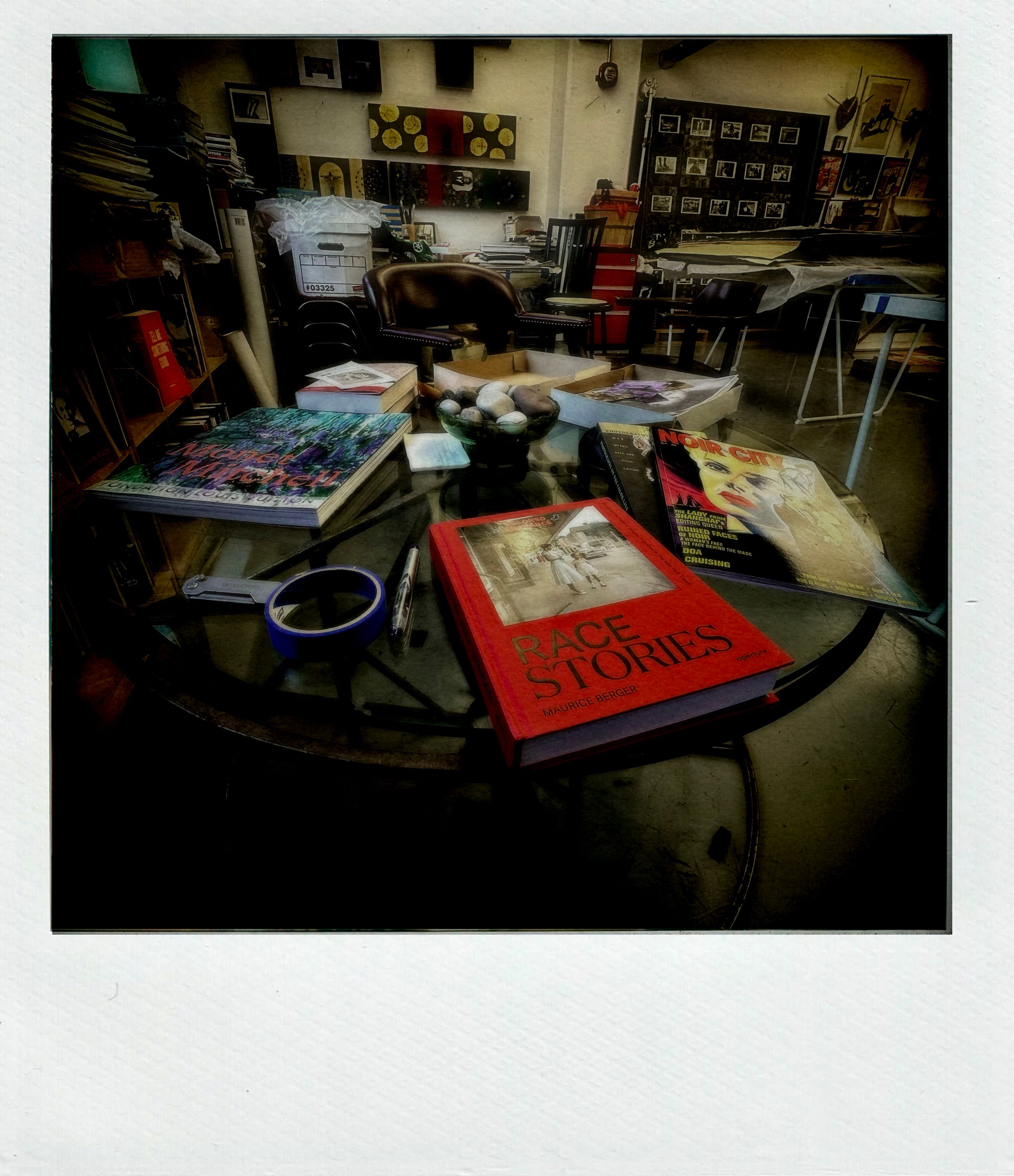 Photograph of studio interior with books and materials on a tabletop, including a book titled "Race Stories"