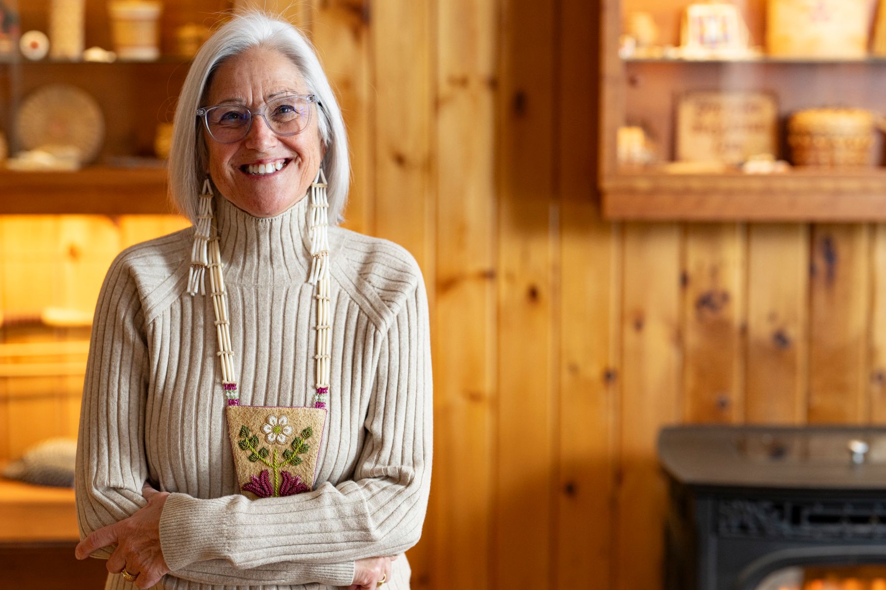 Theresa Secord standing in front of a wood paneled wall featuring shelves displaying baskets and other objects