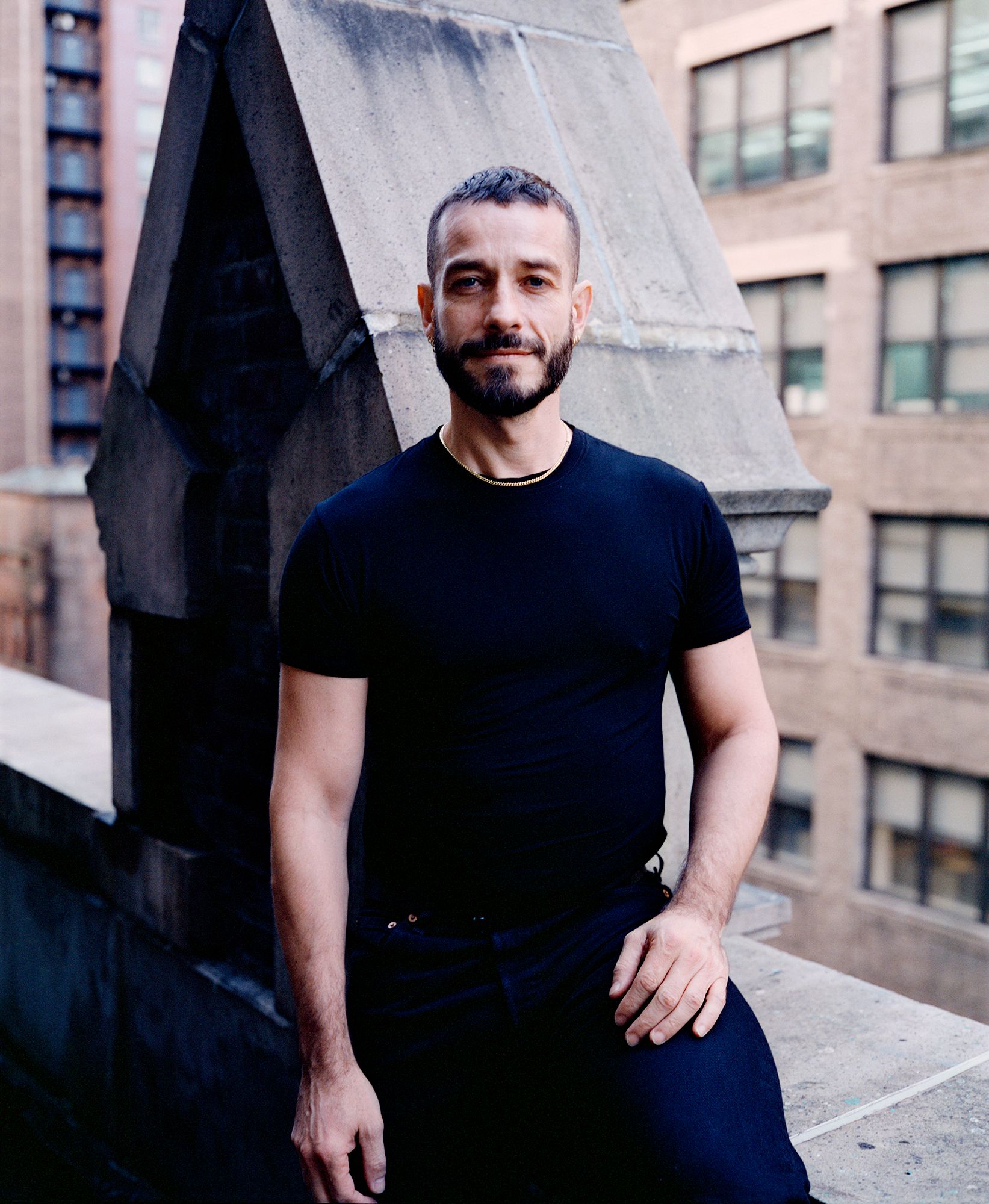 Carlos Motta standing outdoors in front of the architectural detail of a building in an urban setting