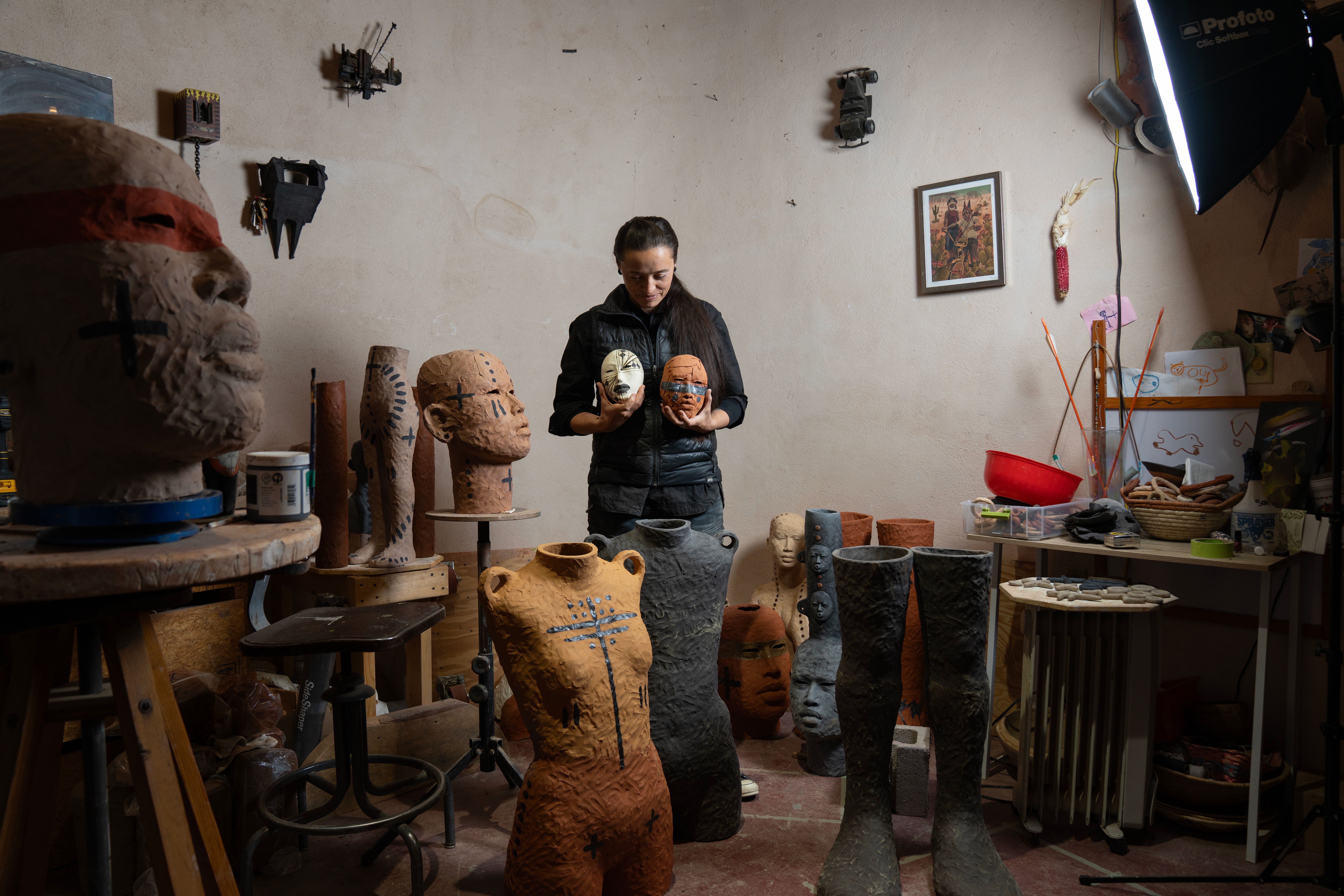 A portrait of Rose holding two ceramic masks in her studio