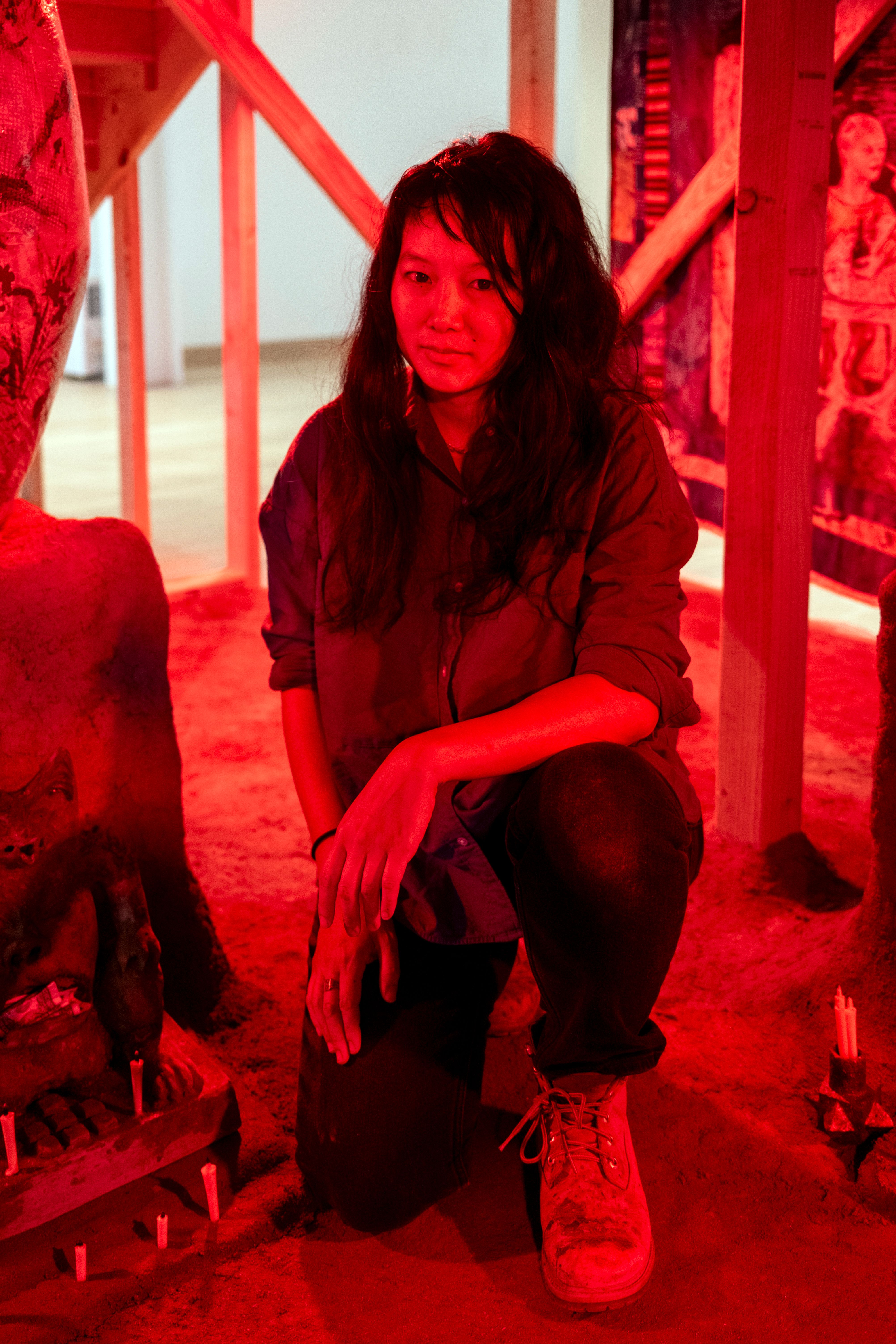 A close up of Candice Lin kneeling next to her work, under all over red light