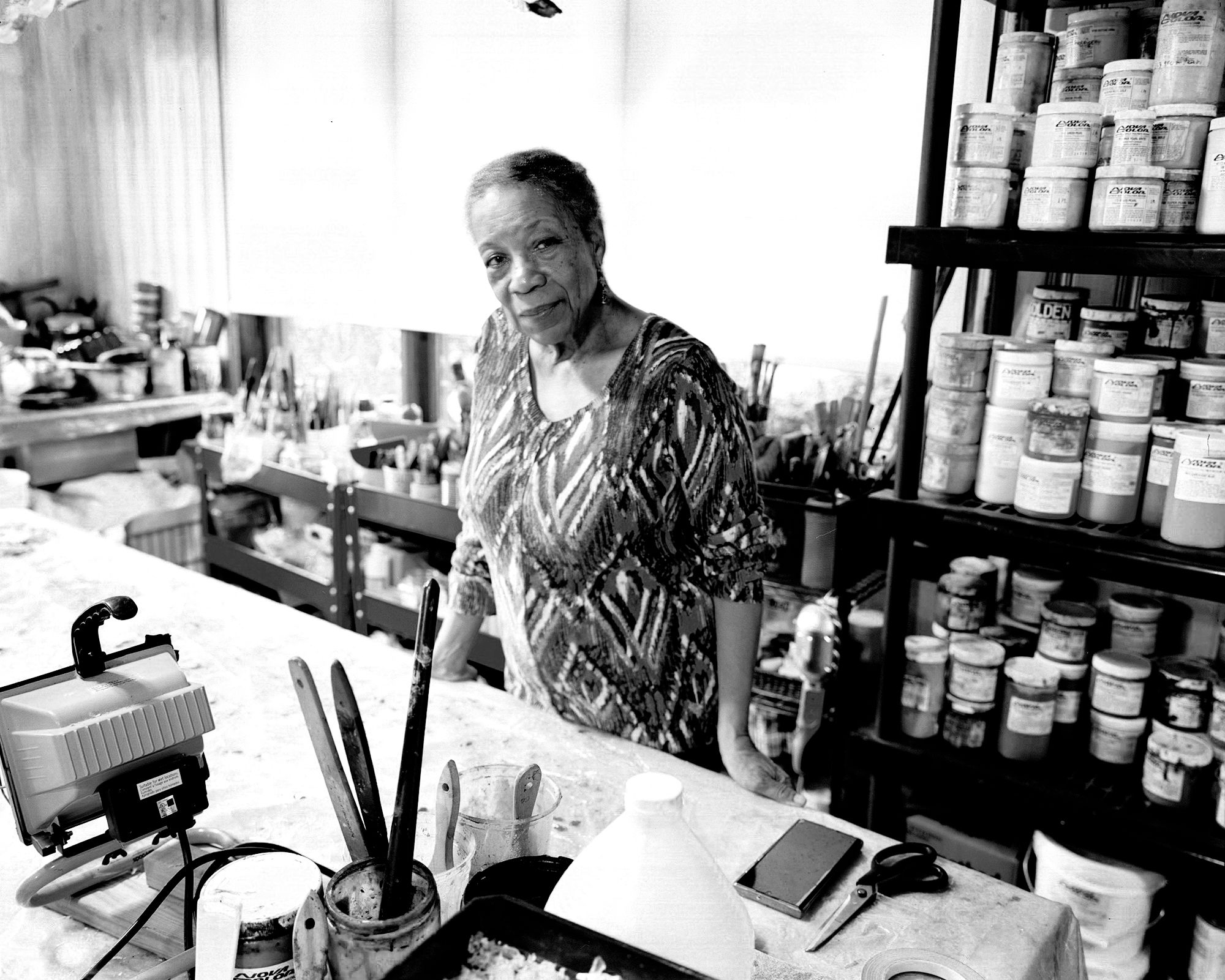 Suzanne Jackson pictured in her studio, surrounded by shelves of paint and other materials