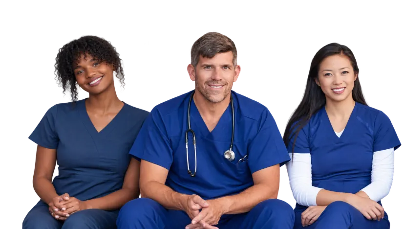 Three healthcare professionals standing together with hands in pockets - a woman in pink scrubs, a woman in green scrubs, and a man in blue scrubs, all wearing stethoscopes