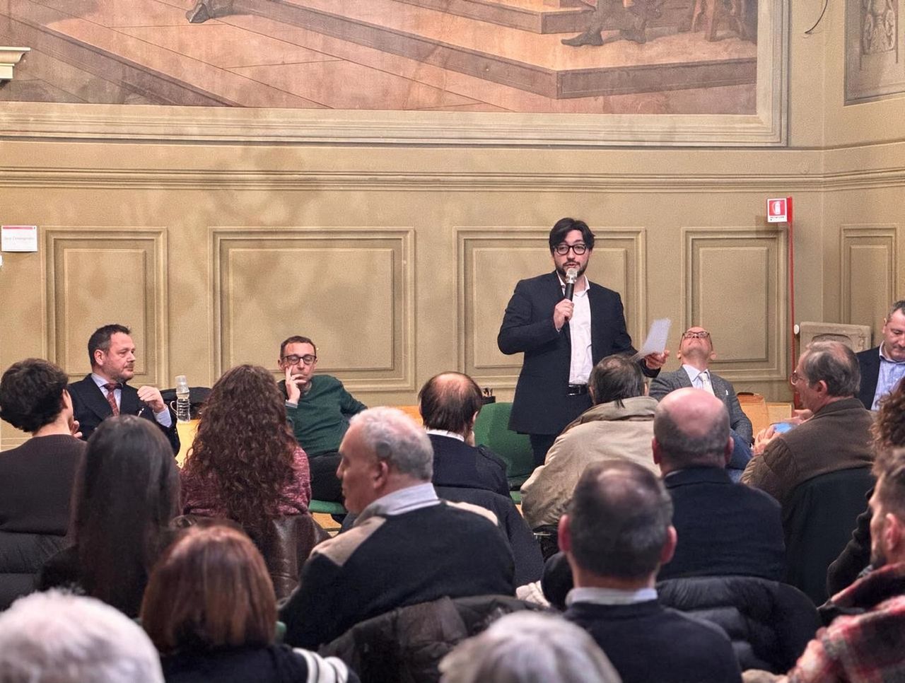 Leonardo Gallozzi parla al microfono davanti a una sala piena durante un incontro pubblico