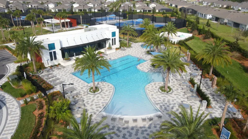 Beautiful outdoor pool surrounded by palm trees, loungers, and sports courts in the background.