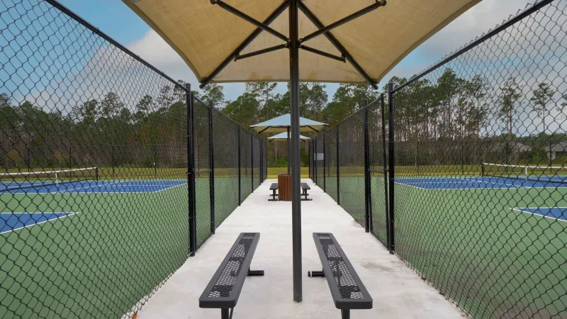 A seating area next to sets of tennis courts featuring benches and shaded umbrellas.