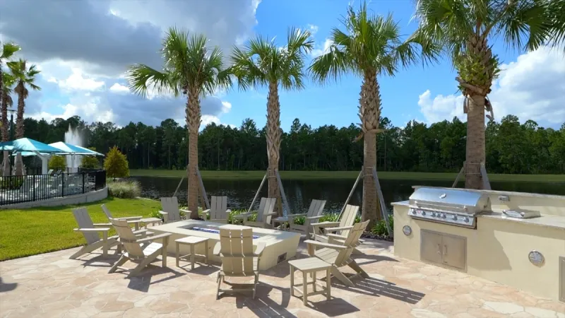 Lakeside outdoor dining area at Del Webb Sunbridge, with a built-in barbecue, offering scenic views for social gatherings.