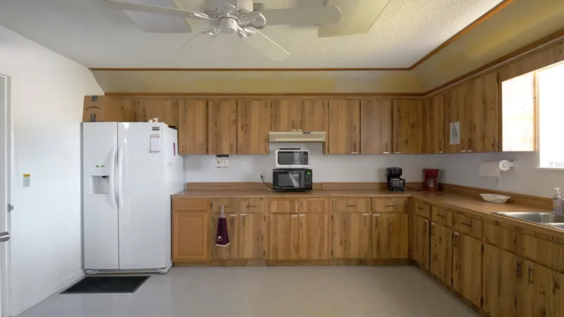A spacious community kitchen area with a refrigerator, a microwave on the counter, and numerous cabinets and drawers providing ample storage space for supplies.