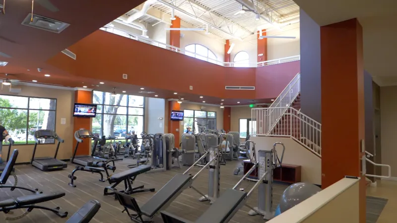 Del Webb Orlando's gym with ample cardio and strength training equipment, TVs for entertainment, and large windows bringing in natural light.