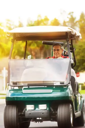 A gentleman smiles while driving a green golf cart.