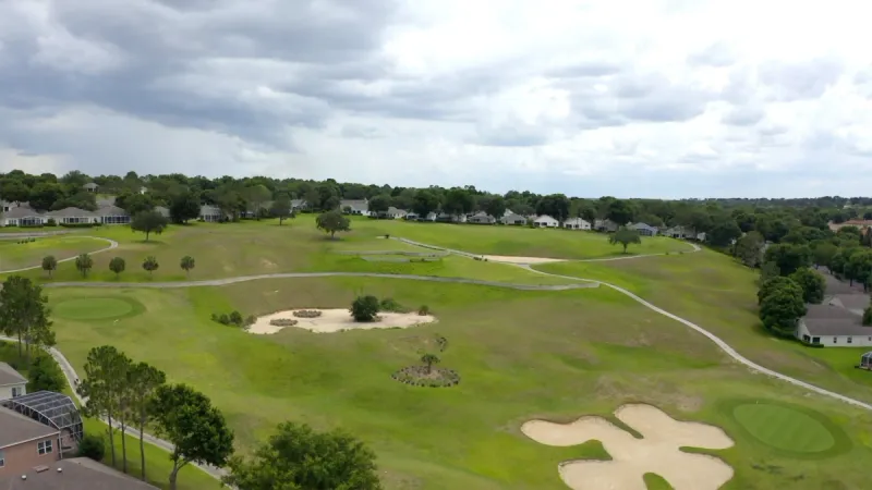Aerial view of a golf course with sand traps and greens, with homes and walking paths along the course.