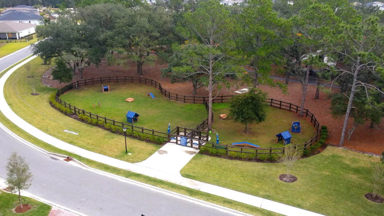 Aerial view of a fenced dog park in a pet-friendly 55+ community, showcasing amenities for pets and their owners.