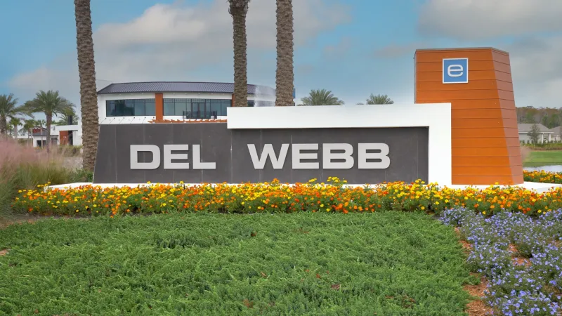 Entrance sign to Del Webb eTown adorned with flower beds and tall palm trees.