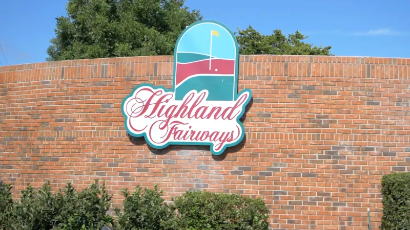 Highland Fairways monument sign on brick wall surrounded by landscaping.