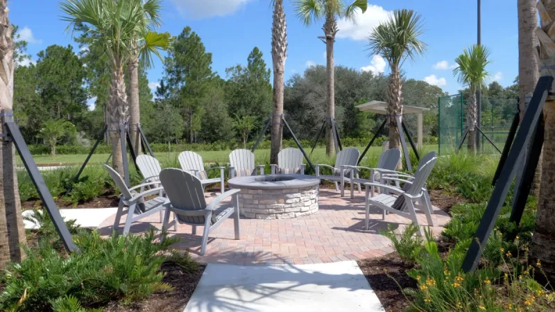 Firepit surrounded by Adirondack chairs and palm trees.