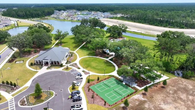 A scenic view of the Summer Bay at Grand Oaks community center, with lively pickleball courts in the foreground, and homes and water features in the background.