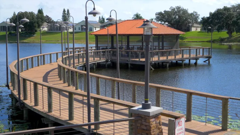 Scenic view of a dock leading to a delightful screened-in gazebo, with Del Webb Orlando homes in the background.