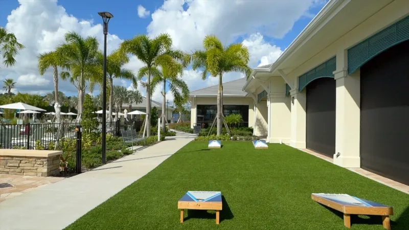 A recreational area with cornhole boards, surrounded by palm trees and the clubhouse at Del Webb Sunbridge.