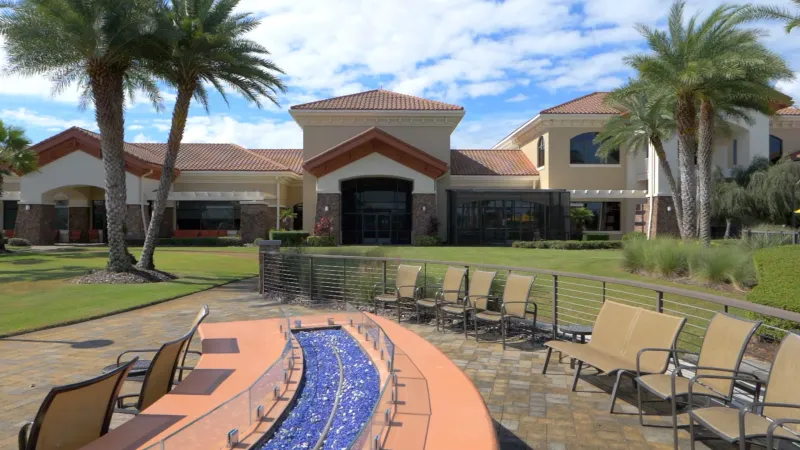 Scenic view of the Del Webb Orlando's clubhouse, showcasing beautiful palm trees, a meticulously manicured lawn, and a cozy firepit surrounded by seating spaces.