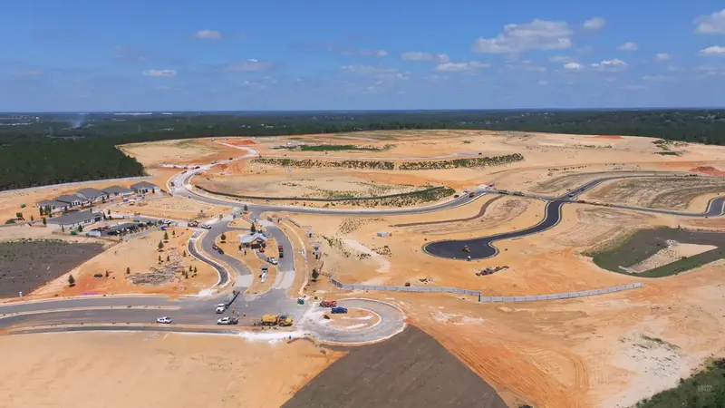 An aerial shot of Del Webb Minneola shows a developing community with new homes, winding roads, and construction in progress under a clear sky.