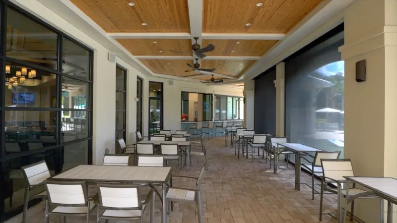 The covered outdoor dining patio of the Hammock Club at Del Webb Sunbridge, with ceiling fans, seating, and views of the lounge.