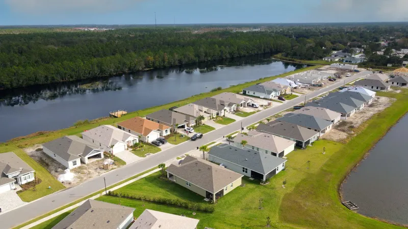 A residential street in Matanzas Lakes with neatly lined homes of various colors, manicured lawns, and a lake with trees.